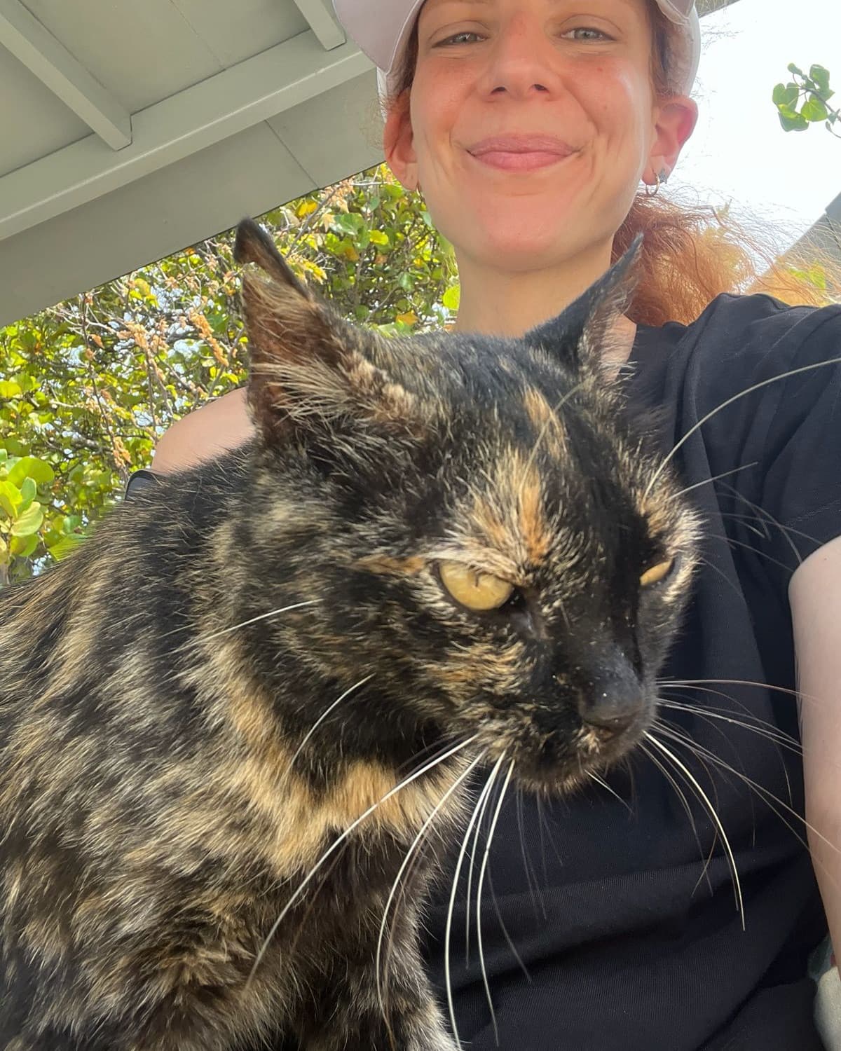 Mujer sonriendo con su gata carey en brazos al aire libre